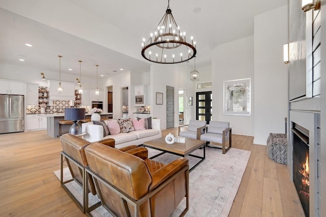 125 Reataway Dr, Dripping Springs, TX 78620 - living room featuring light wood-style floors, a towering ceiling, a warm lit fireplace, a chandelier, and recessed lighting