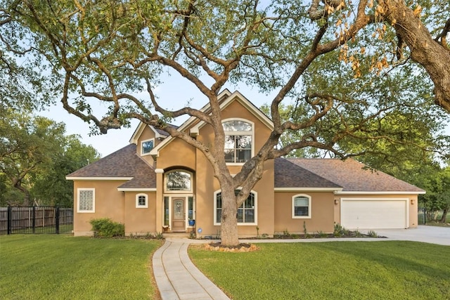 traditional-style home with a front lawn, driveway, fence, a garage, and stucco siding