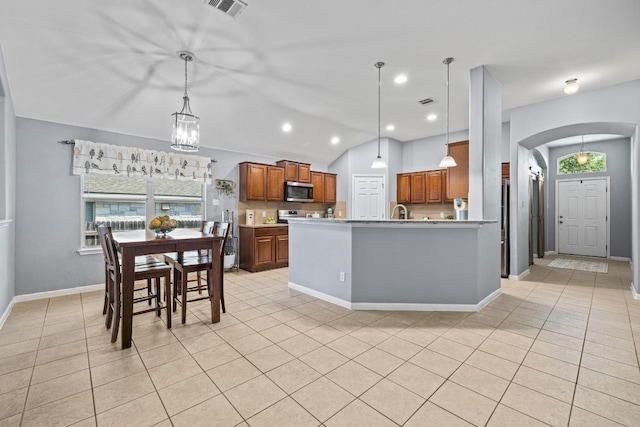 1416 Muddy Waters Dr, Pflugerville, TX 78660 - kitchen featuring stainless steel microwave, arched walkways, brown cabinets, light tile patterned floors, and lofted ceiling