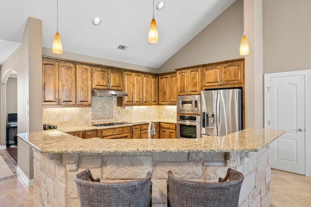 604 Lake Side Cv, Georgetown, TX 78628 - kitchen featuring stainless steel appliances, arched walkways, light stone counters, brown cabinetry, and high vaulted ceiling