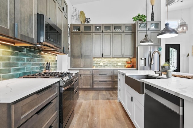 kitchen featuring stainless steel appliances, a sink, light wood-style floors, light stone countertops, and hanging light fixtures