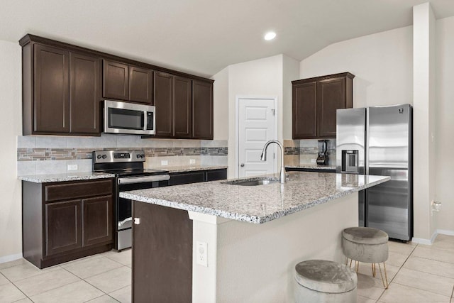 kitchen with stainless steel appliances, a sink, dark brown cabinetry, light tile patterned flooring, and vaulted ceiling