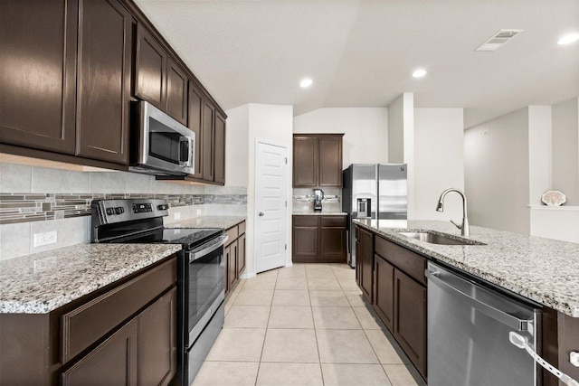 kitchen featuring appliances with stainless steel finishes, a sink, tasteful backsplash, dark brown cabinetry, and lofted ceiling