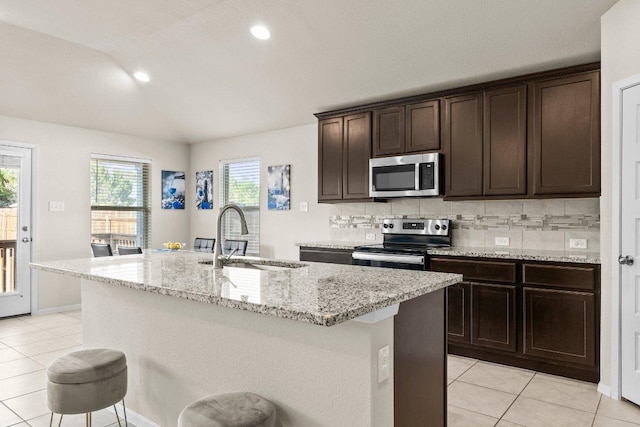kitchen with stainless steel appliances, a sink, light tile patterned floors, a center island with sink, and recessed lighting