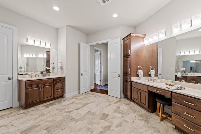 full bath featuring two vanities, a sink, visible vents, and baseboards
