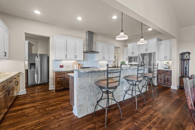 kitchen with stainless steel appliances, dark wood finished floors, a kitchen bar, decorative backsplash, and wall chimney range hood