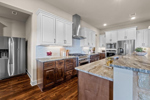 kitchen with wall chimney exhaust hood, visible vents, high quality appliances, and white cabinetry