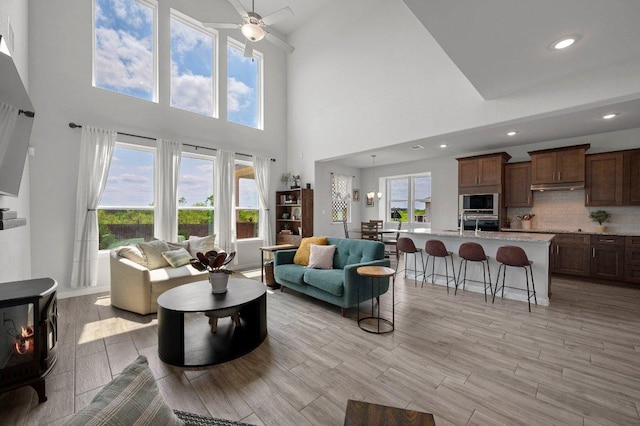 living room with recessed lighting, light wood-type flooring, a ceiling fan, and high vaulted ceiling