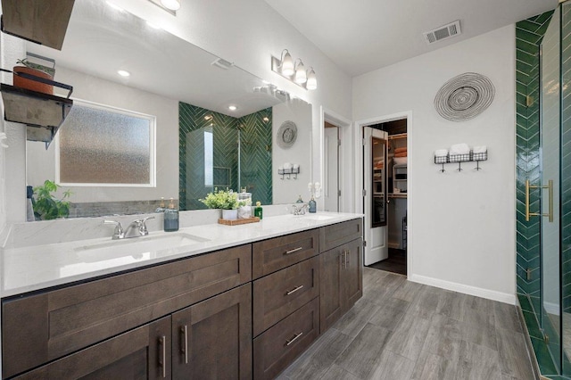 full bathroom featuring double vanity, wood finished floors, visible vents, a sink, and a walk in closet