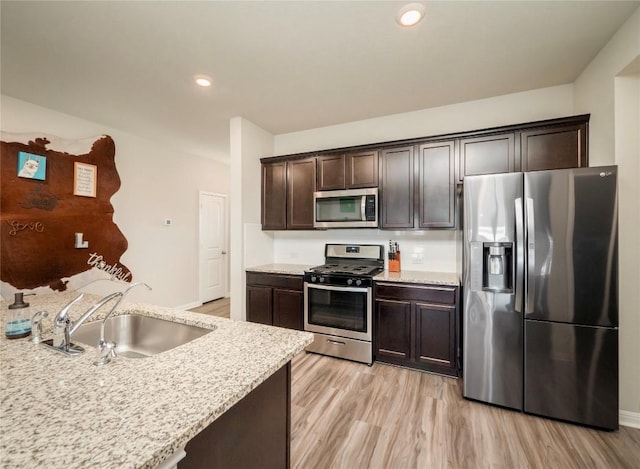 369 Empress Tree Dr, Leander, TX 78641 - kitchen with appliances with stainless steel finishes, a sink, dark brown cabinets, light wood finished floors, and light stone counters