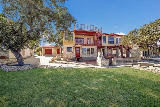 rear view of property with driveway, stone siding, a lawn, an attached garage, and a balcony