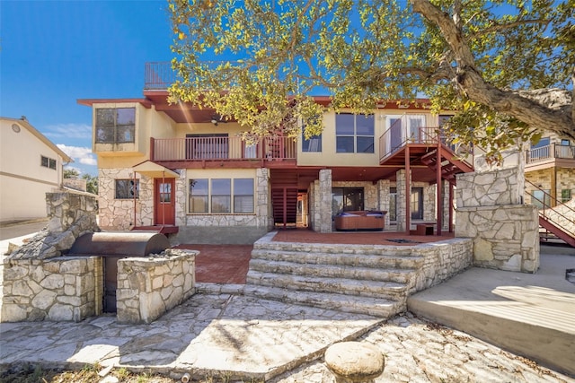 multi unit property with stone siding, a hot tub, a balcony, a patio, and stucco siding