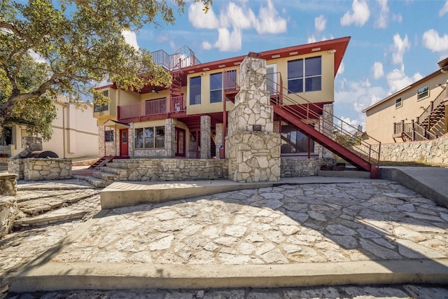 rear view of property with stucco siding, stone siding, stairs, and a balcony