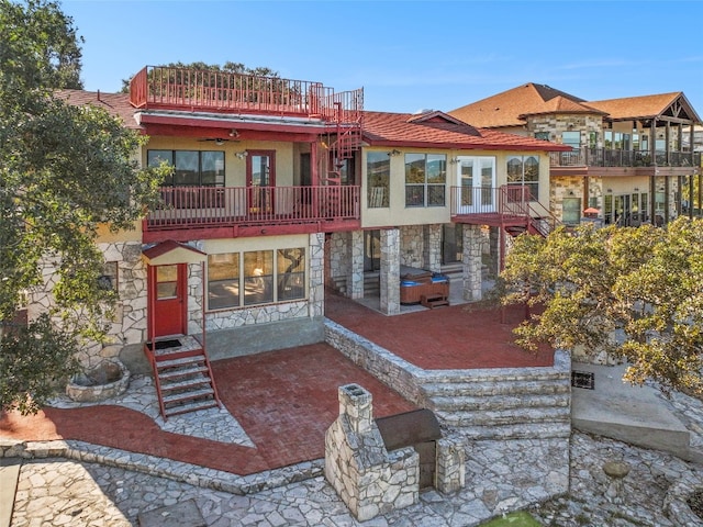 rear view of property featuring stone siding, a balcony, a patio, stucco siding, and a jacuzzi