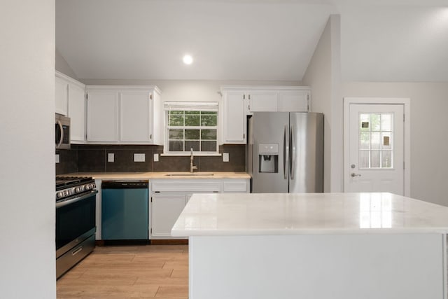 kitchen with a sink, vaulted ceiling, backsplash, light wood-style floors, and appliances with stainless steel finishes