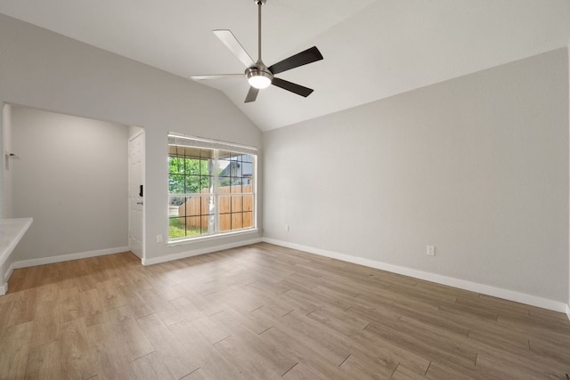 spare room featuring baseboards, lofted ceiling, a ceiling fan, and light wood-type flooring