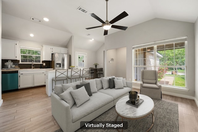 living area featuring lofted ceiling, visible vents, light wood finished floors, and a ceiling fan