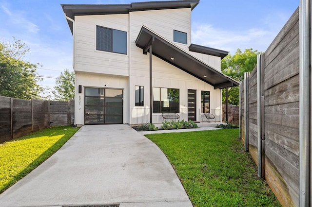 view of front facade featuring board and batten siding, a fenced backyard, a front yard, and concrete driveway