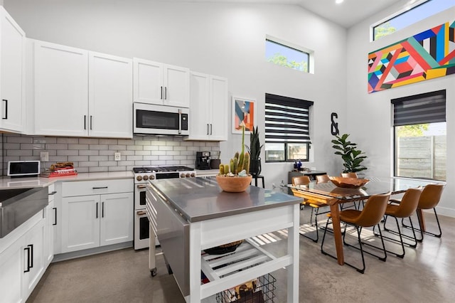 kitchen featuring finished concrete floors, white microwave, decorative backsplash, a high ceiling, and range with two ovens