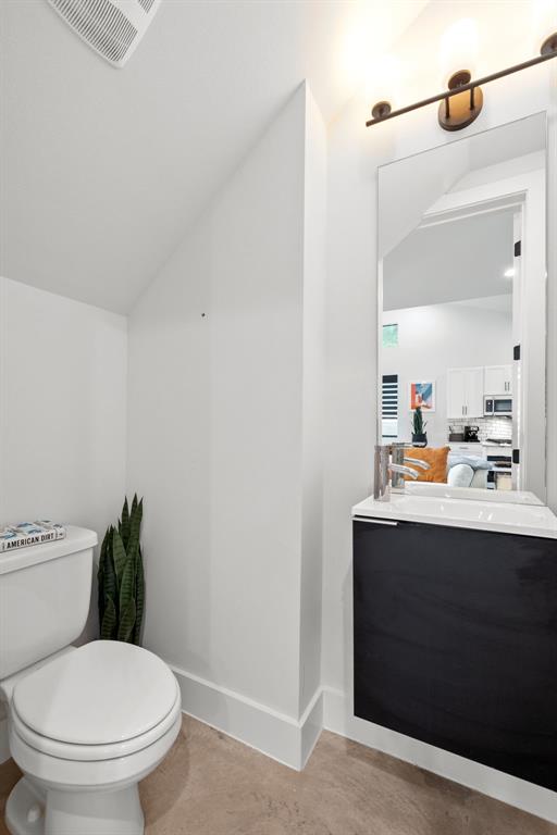 half bath featuring lofted ceiling, visible vents, toilet, vanity, and baseboards