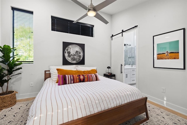 bedroom with a barn door, ensuite bathroom, baseboards, wood finished floors, and ceiling fan