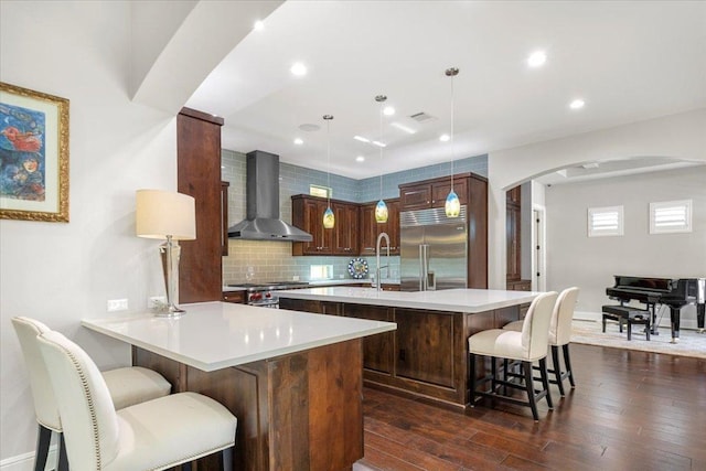 205 Bisset Ct, Austin, TX 78738 - kitchen with wall chimney range hood, stainless steel appliances, arched walkways, a breakfast bar, and light countertops