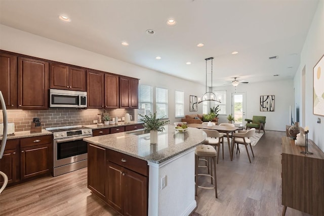 9945 Comely Bnd, Manor, TX 78653 - kitchen with stainless steel appliances, open floor plan, a kitchen island, light stone countertops, and recessed lighting