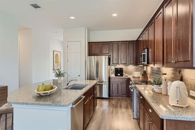 9945 Comely Bnd, Manor, TX 78653 - kitchen featuring appliances with stainless steel finishes, a sink, light wood finished floors, backsplash, and light stone countertops