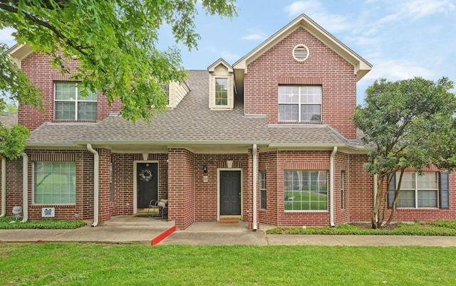 view of front facade with brick siding, a patio area, a shingled roof, and a front lawn