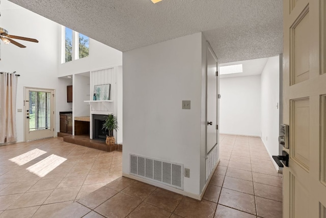 hallway with light tile patterned floors, a textured ceiling, a towering ceiling, and baseboards
