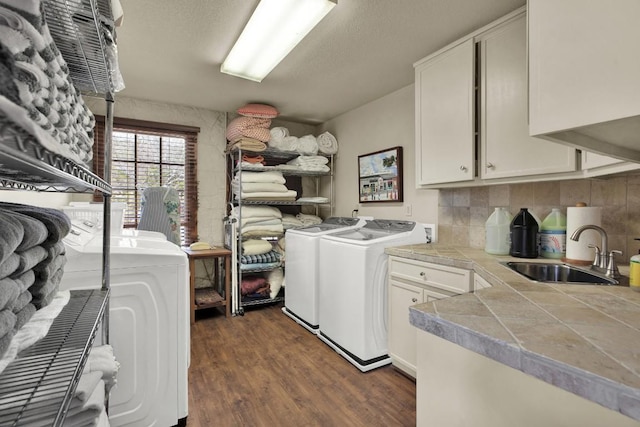 laundry area featuring washing machine and clothes dryer, cabinet space, a sink, and dark wood-style flooring