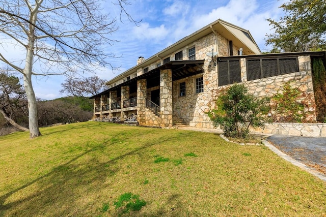 back of house featuring stone siding, a lawn, and a chimney