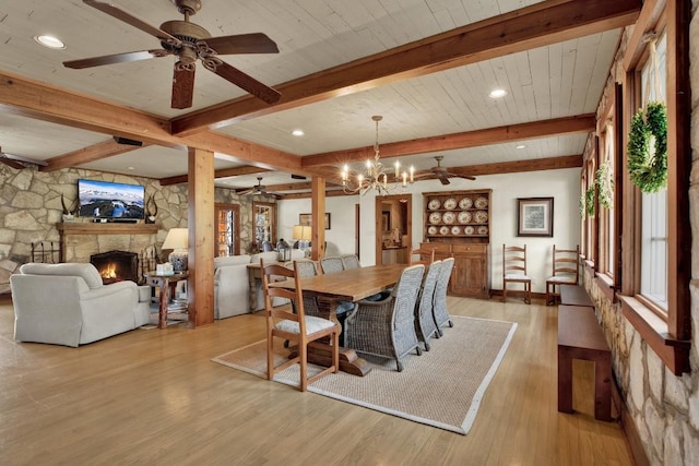 dining area with ceiling fan with notable chandelier, a fireplace, beamed ceiling, and a healthy amount of sunlight