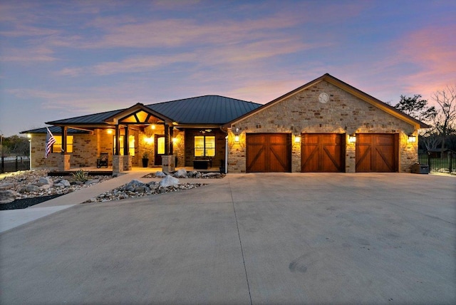 view of front of property featuring driveway, a porch, stone siding, metal roof, and a garage