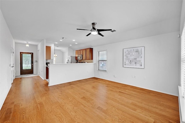 unfurnished living room featuring light wood-style floors, a healthy amount of sunlight, a ceiling fan, and baseboards