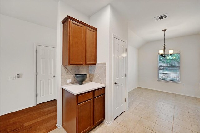 5705 Zachary Scott St, Austin, TX 78747 - kitchen with brown cabinets, light countertops, a chandelier, decorative backsplash, and lofted ceiling