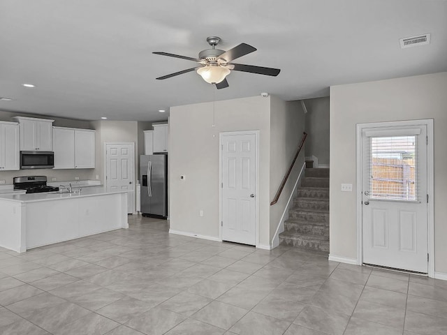 interior space featuring stairs, a sink, ceiling fan, baseboards, and visible vents