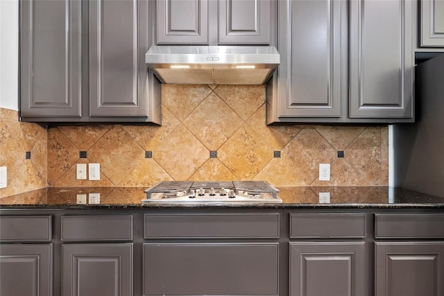 kitchen with stainless steel gas cooktop, dark stone counters, decorative backsplash, under cabinet range hood, and gray cabinetry
