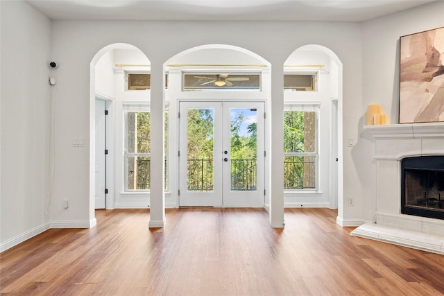 entryway featuring a fireplace with raised hearth, wood finished floors, a ceiling fan, arched walkways, and french doors