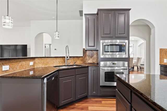 kitchen featuring dark stone counters, a sink, stainless steel appliances, a peninsula, and arched walkways