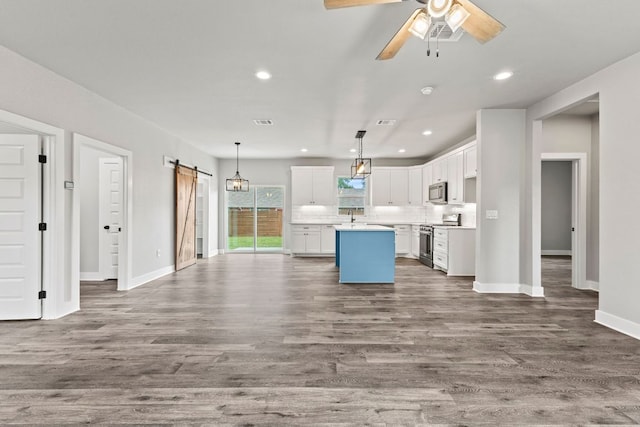 kitchen with a barn door, white cabinets, recessed lighting, stainless steel appliances, and a kitchen island