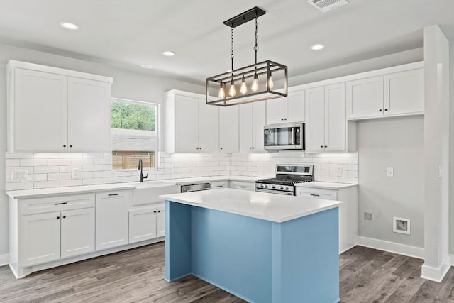 kitchen with a sink, light wood-type flooring, decorative backsplash, appliances with stainless steel finishes, and white cabinetry