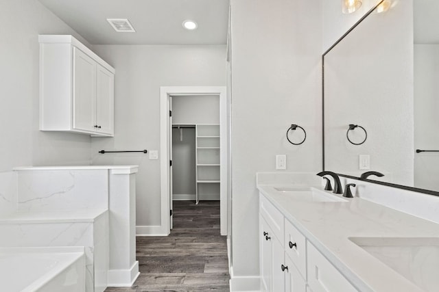 bathroom featuring a sink, double vanity, visible vents, wood finished floors, and a garden tub