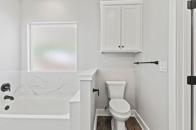 bathroom featuring a bath, toilet, baseboards, and wood finished floors
