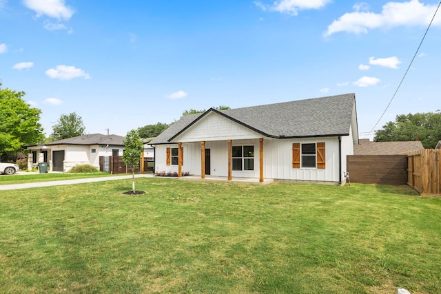 view of front facade with board and batten siding, roof with shingles, a front yard, and fence