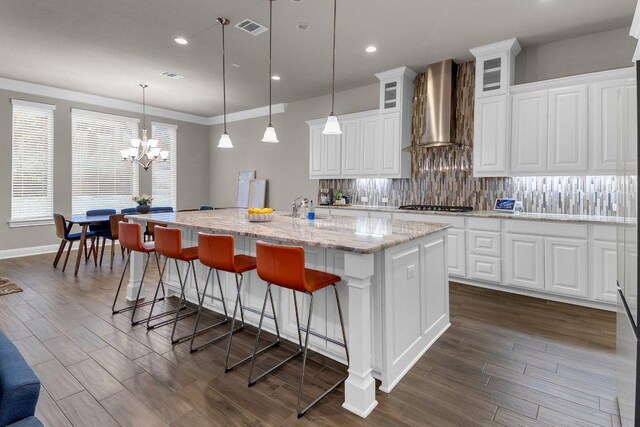 2601 Montebelluna Pl, Leander, TX 78641 - kitchen with wall chimney range hood, decorative backsplash, a kitchen island with sink, white cabinetry, and glass insert cabinets