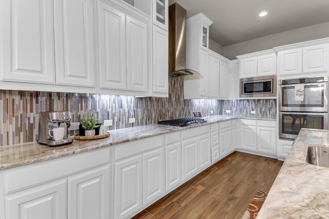 2601 Montebelluna Pl, Leander, TX 78641 - kitchen with wall chimney range hood, appliances with stainless steel finishes, white cabinetry, backsplash, and dark wood-style flooring