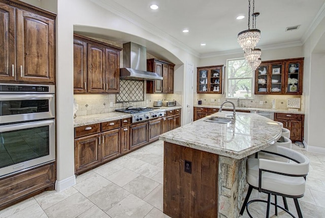 kitchen with wall chimney range hood, a kitchen breakfast bar, a sink, stainless steel appliances, and visible vents