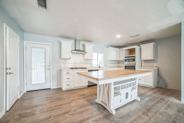 kitchen featuring wall chimney range hood, visible vents, tasteful backsplash, appliances with stainless steel finishes, and white cabinetry