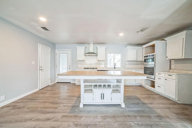 kitchen with decorative backsplash, double oven, light countertops, wall chimney exhaust hood, and visible vents